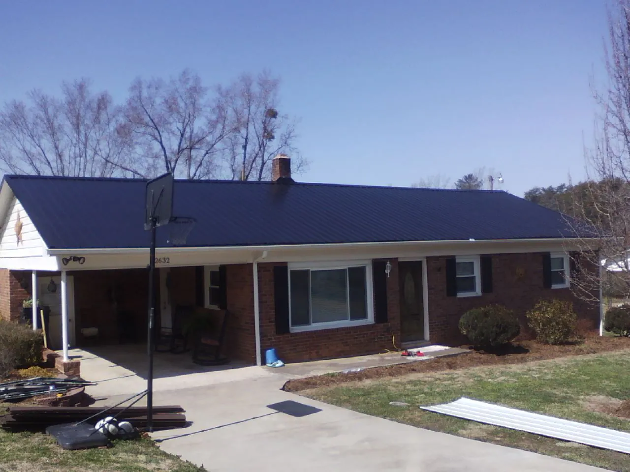 Finished dark blue metal roof on a brick ranch with a carport in Glenpool