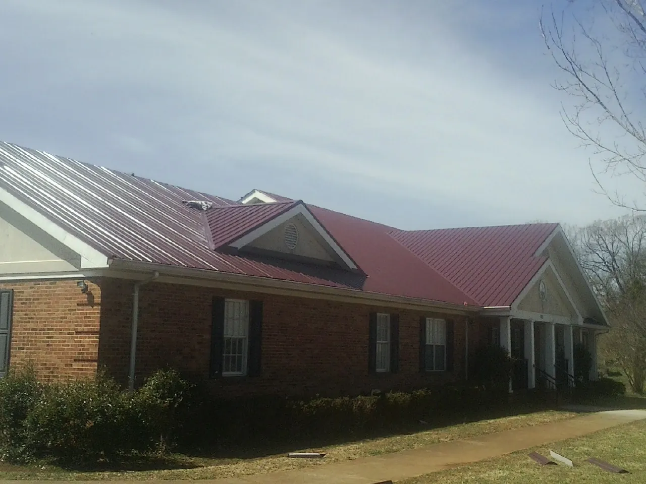 Red metal roof with gabled entries on a long brick building, from a Hail Damage Roof Repair job in Glenpool