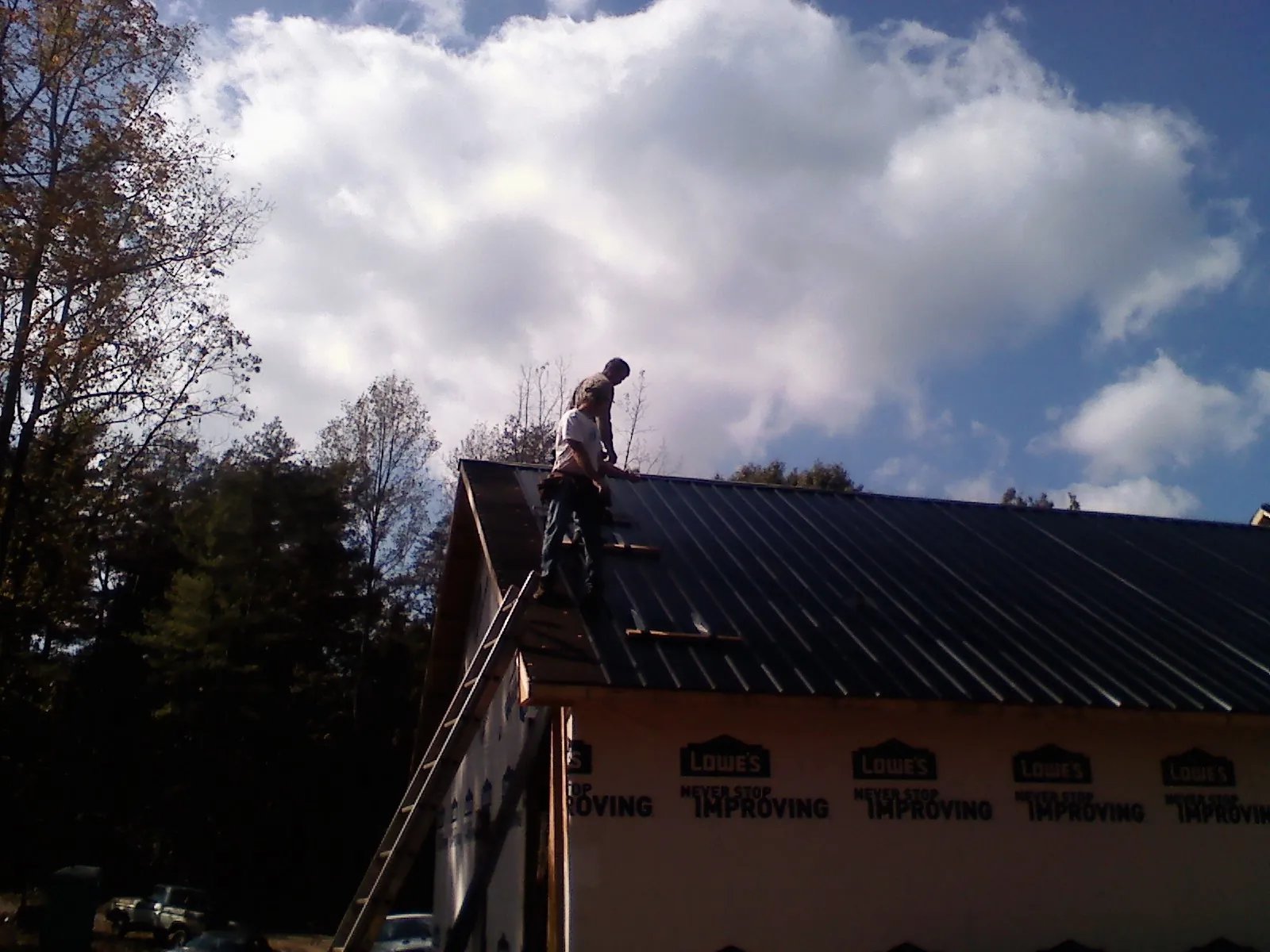 Roofer fastening dark metal panels high against a cloudy sky, from a Roof Inspection job in Glenpool