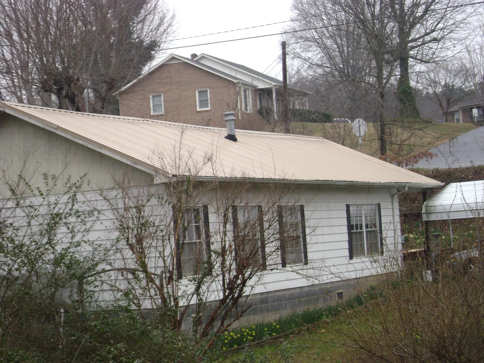 Tan metal roof on a white sided house set into a hillside — Commercial Roofing by Roofing Brothers in Glenpool