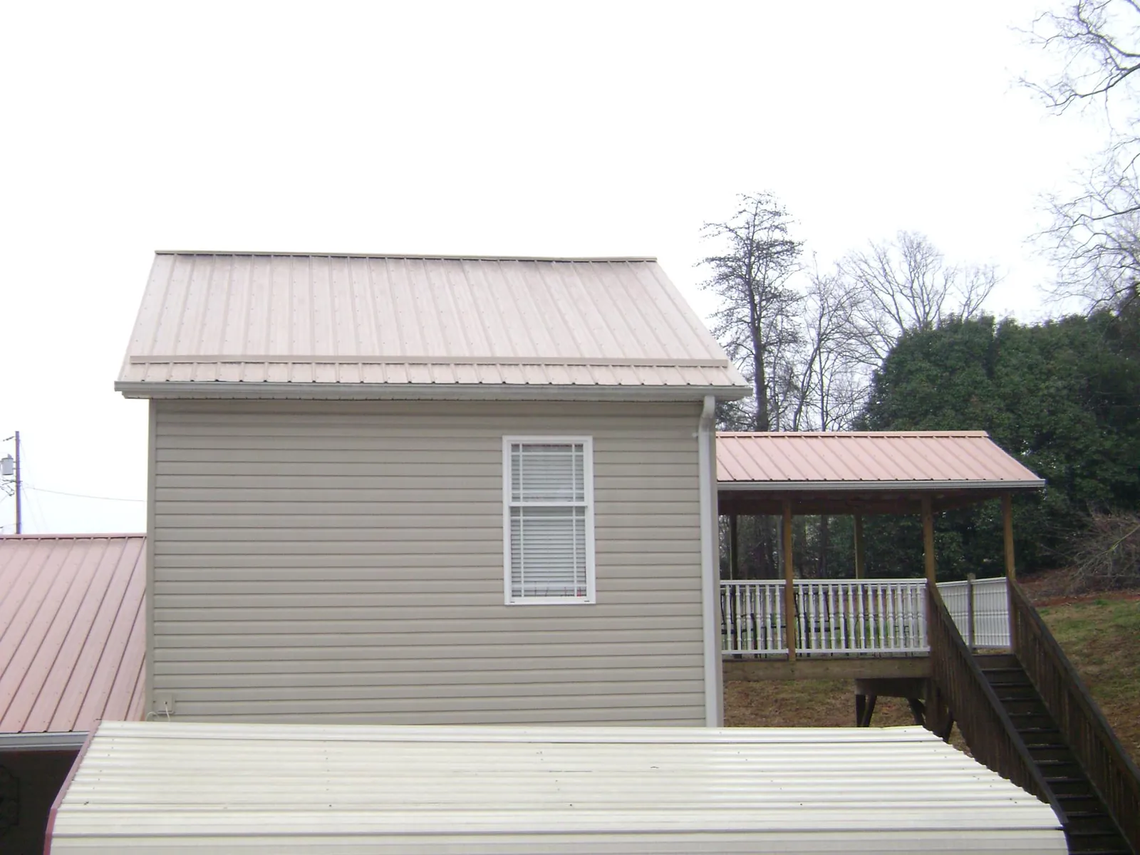 Tan metal roofs on a two story addition and attached porch, from a Roof Replacement job in Glenpool