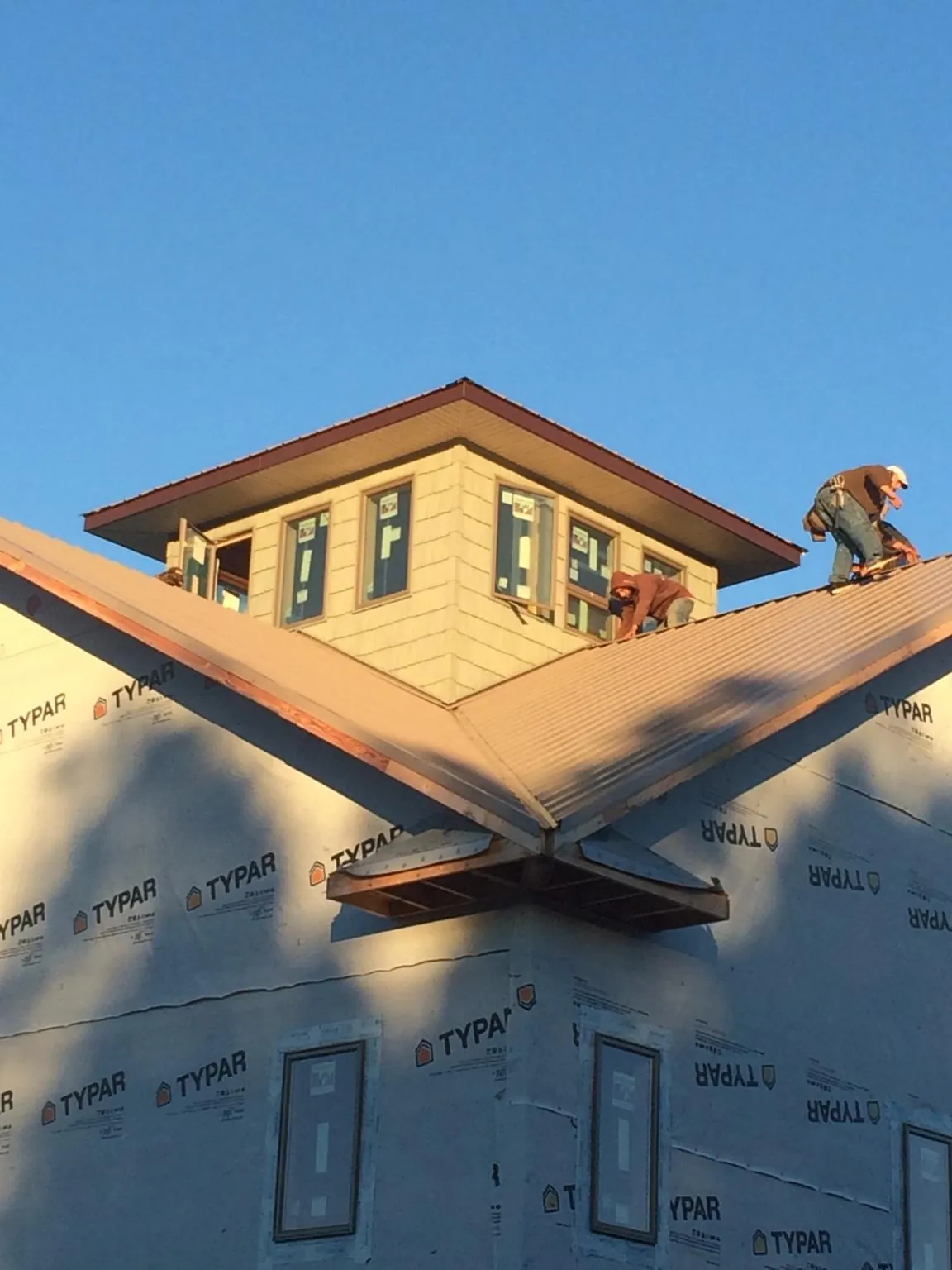 Roofers working around a rooftop cupola on a new metal roof at sunset — Roof Waterproofing in Glenpool by Roofing Brothers